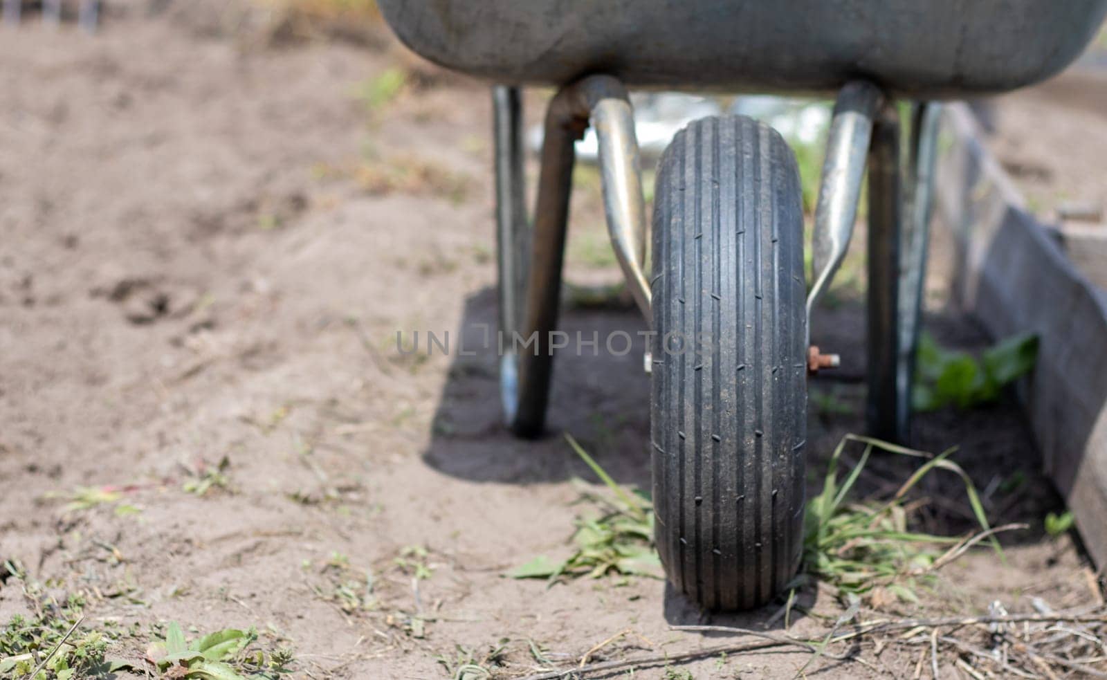 Gray metal garden wheelbarrow with two handles and one wheel. The wheelbarrow is in the garden or garden. Gardener's wheelbarrow in the backyard. Garden cleaning