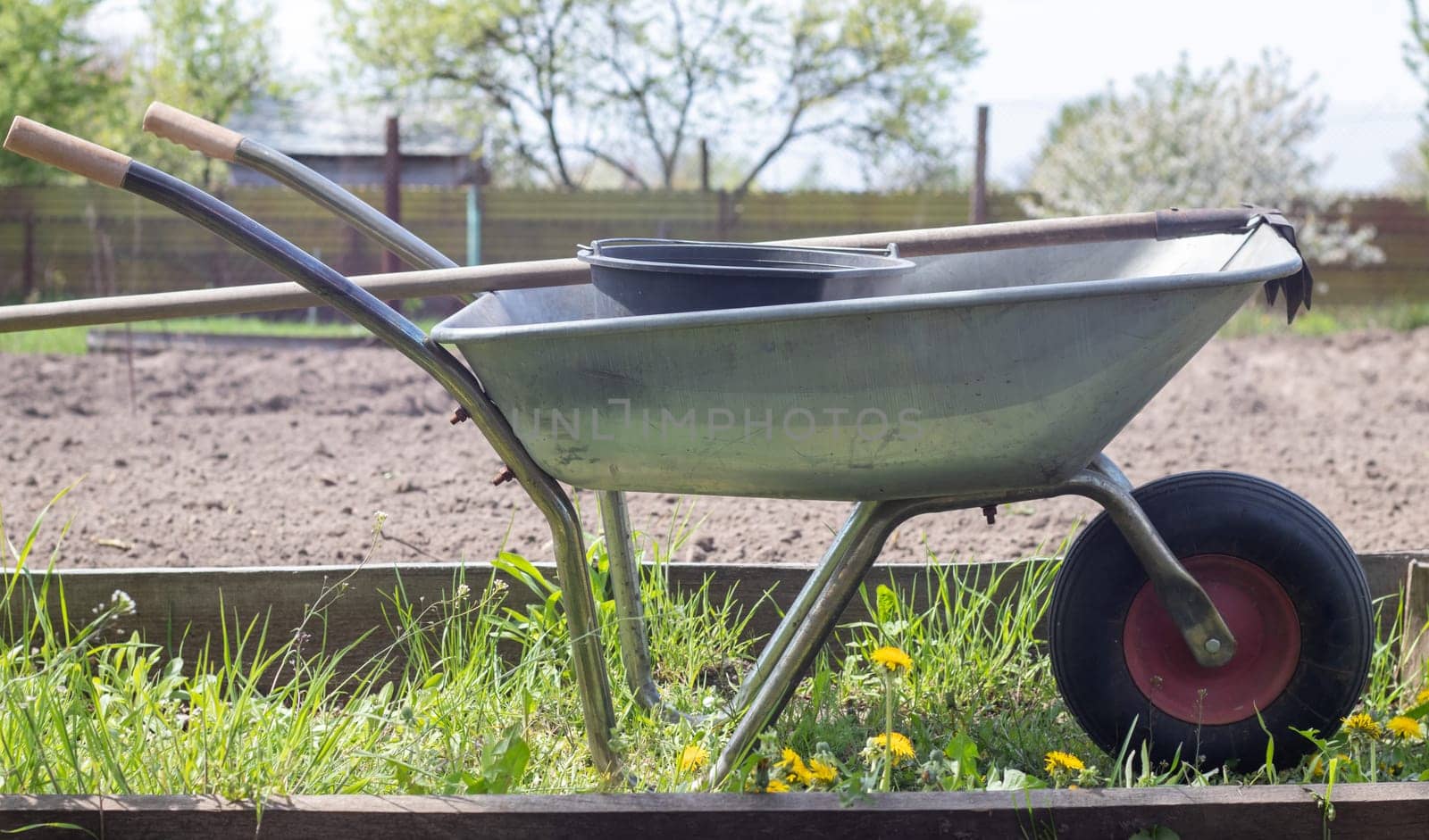 Gray metal garden wheelbarrow with two handles and one wheel. The wheelbarrow is in the garden or garden. Gardener's wheelbarrow in the backyard. Garden cleaning