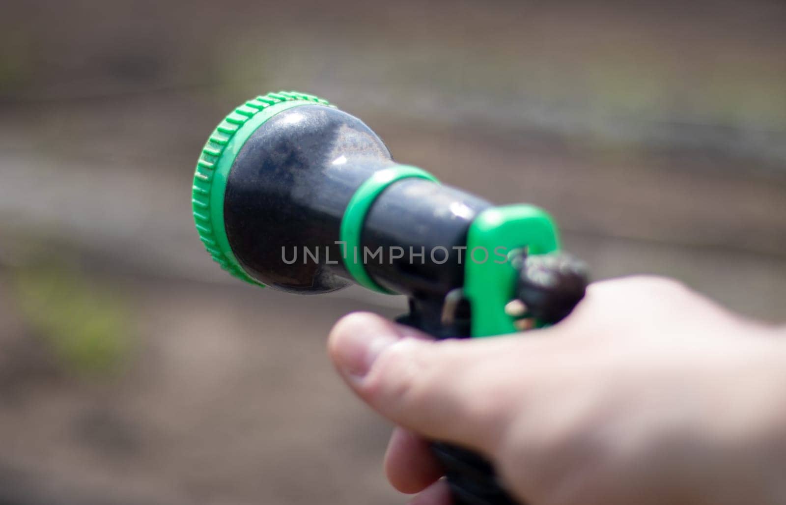 The gardener's hand holds a hose with a sprayer and waters the plants in the garden. Green atomizer in hand with a large lan. Horticulture hobby concept. Watering with a hose