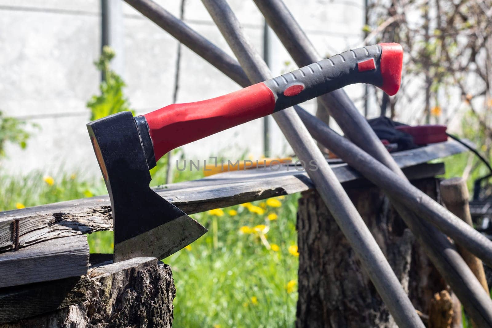 An ax with a red handle plunges into a stump. Sawmill operation concept. Woodworking. Stump and ax in sunny weather. Preparing firewood for the winter. Selective focus, blurred background
