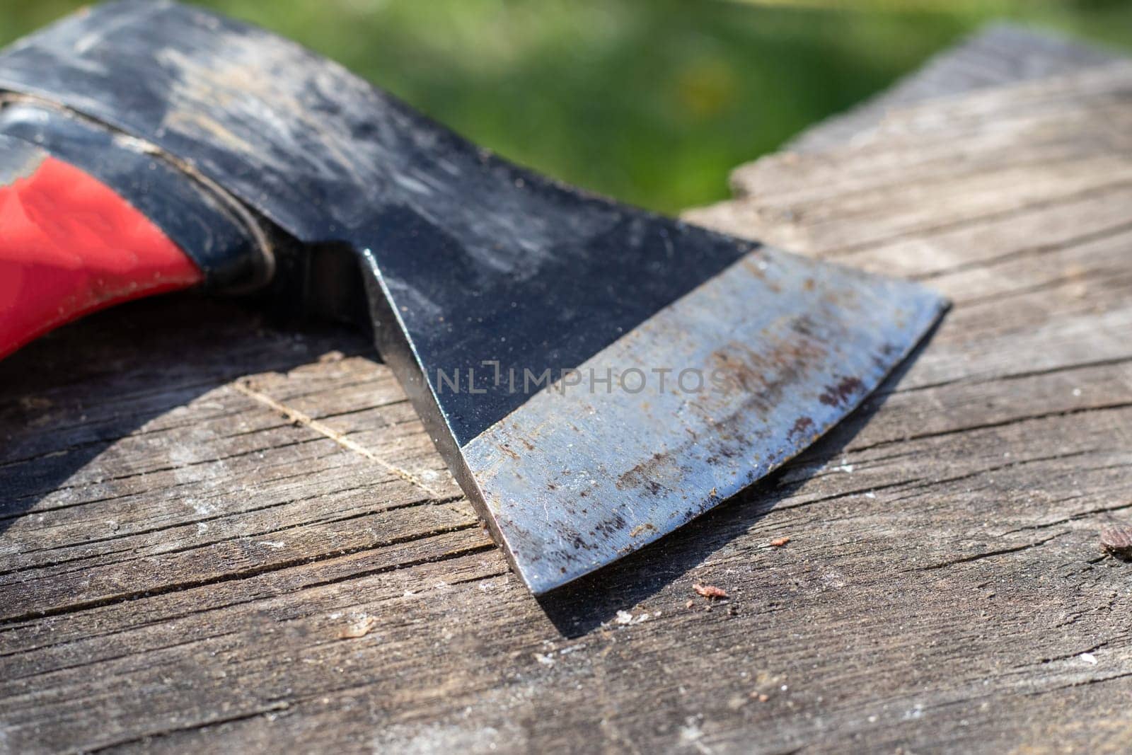 A sharp ax with an ergonomic rubberized handle on a wooden background. The ax is intended for rough, rough processing of wood. Has a forged heat treated carbon steel wedge