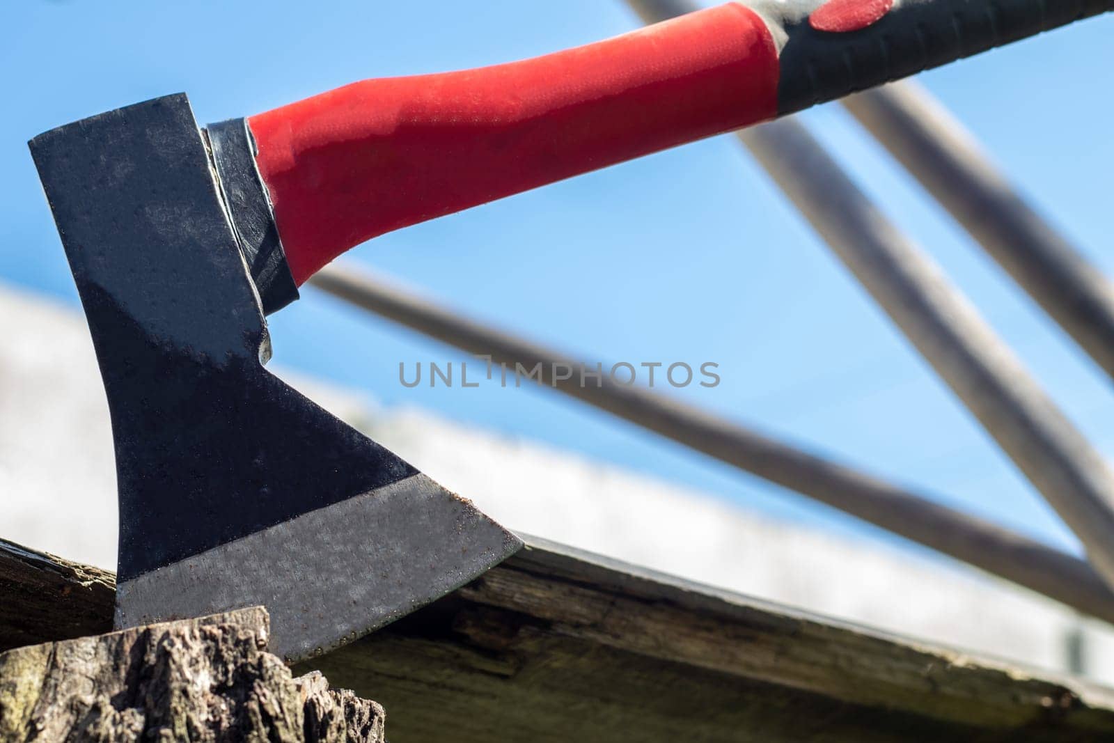 A new modern ax with a red handle sticks out of a wooden stump against a green meadow on a summer sunny day. The ax stuck into the stump. Ax blade in a log