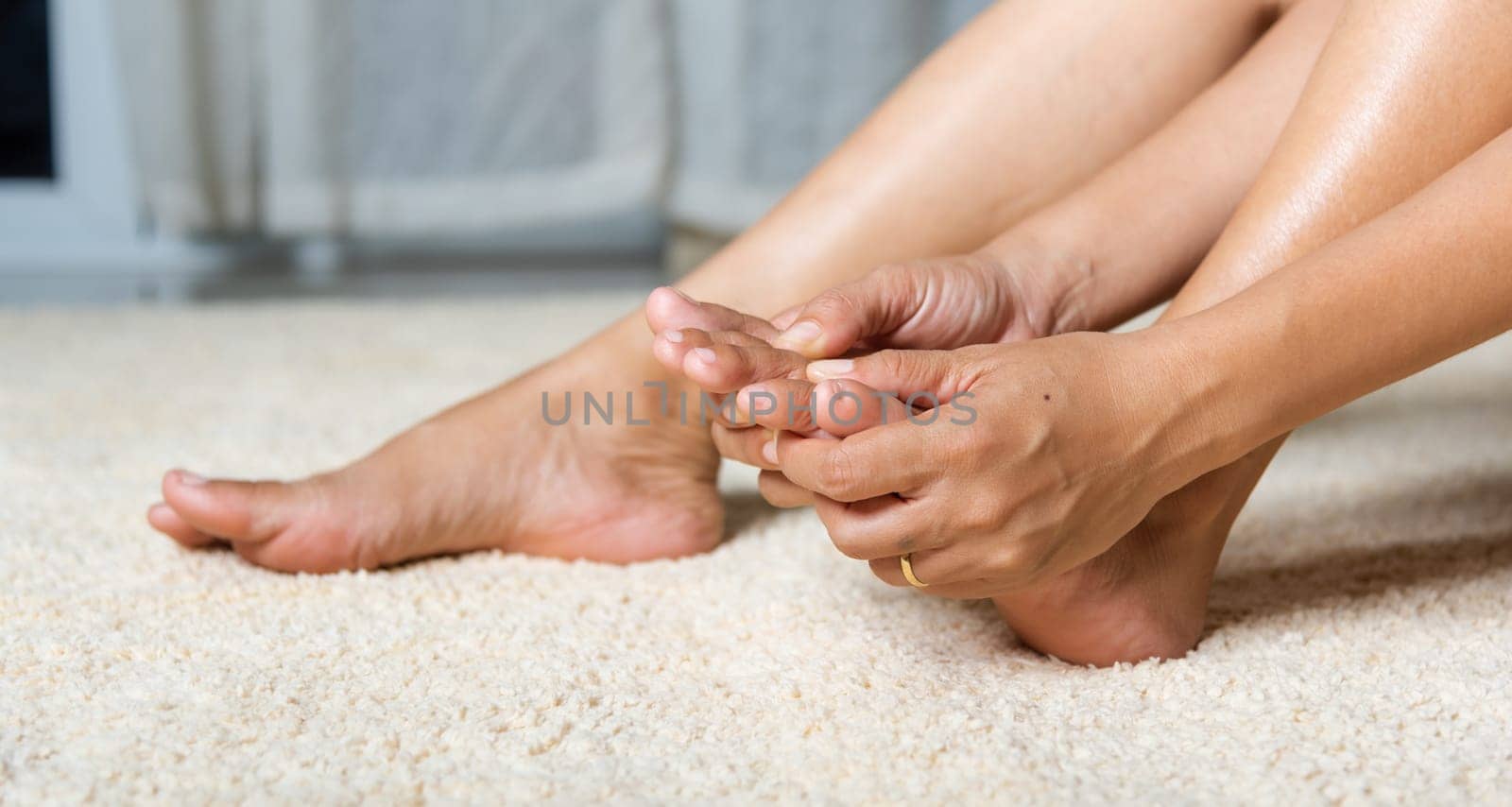 Foot pain, Asian woman holds her toe injury feeling pain her foot at home, female suffering from feet ache use hand massage relax muscle from toe in house interior, Healthcare problems medical concept