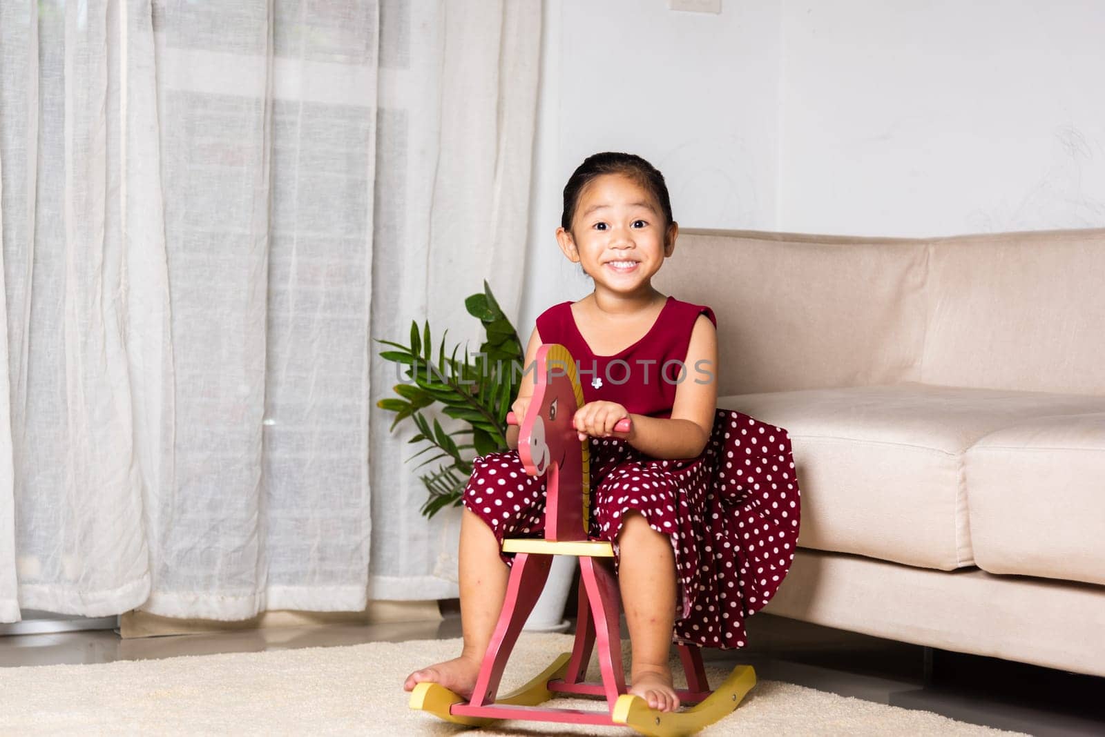 Asian cute little girl swinging riding toy horse, Smiling kid playing horse rocking chair at home in living room, Happy time to play during self kindergarten preschool