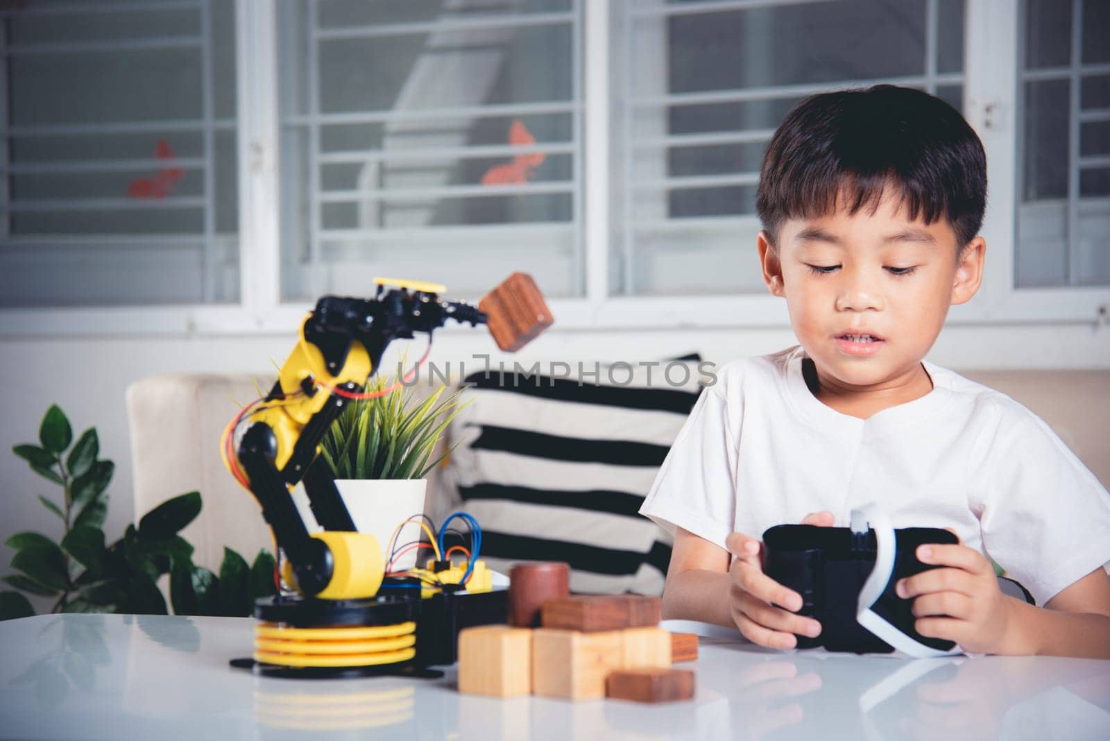 Happy Asian little kid boy using remote control playing robotic machine arm for pick up wood block, Funny child learning successful getting lesson control robot arm, Technology science education