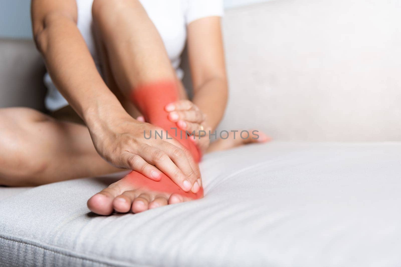 Foot pain, Asian woman sitting on sofa hold her ankle injury feeling pain in her foot at home, female suffering from feet ache use hand massage relax muscle from ankle interior, Healthcare and medical