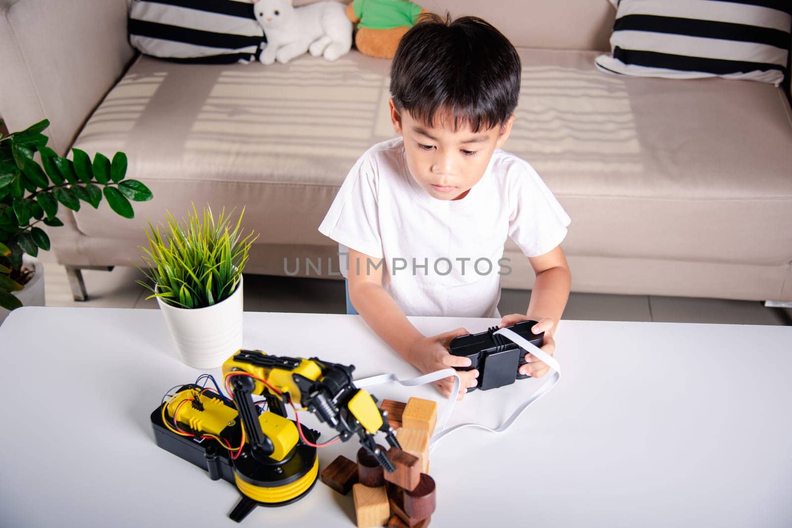 Happy Asian little boy using remote control playing robotic machine arm for pick up wood block, Funny learning successful getting a lesson control robot arm, Technology science education concept