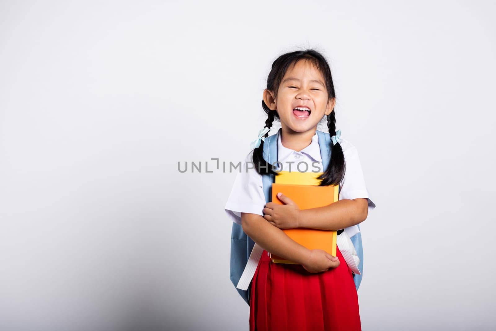 Asian adorable toddler smiling happy wear student thai uniform red skirt stand hold or hugging book in studio shot isolated on white background, Portrait little children girl preschool, Back to school