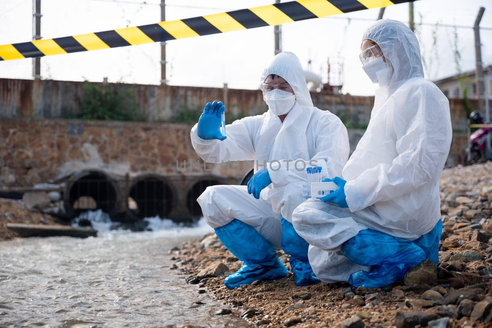 Ecologist sampling water from the river with test tube, Scientist or Biologist in a protective suit and protect mask collects sample of waste water from industrial for analyze, problem environment