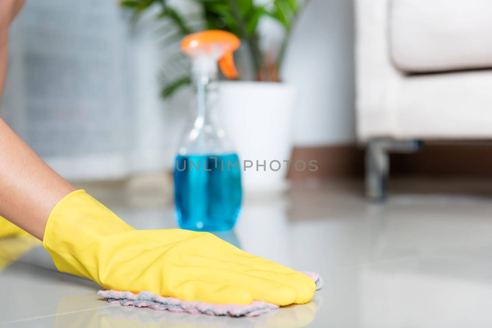 Asian woman wearing yellow rubber glover with cloth rag and detergent spray cleaning floor at home in living room, Female hands wash cleaner, housework and housekeeping concept