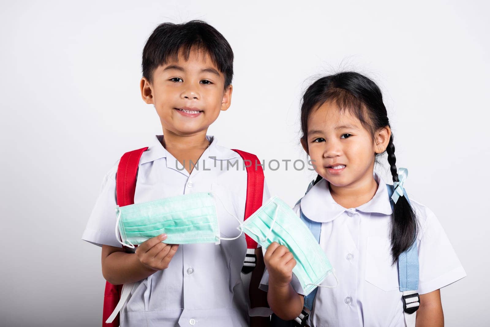 Two Asian student kid girl boy brother sister wearing student thai uniform holding protect mask ready to go to school in studio shot isolated on white background, new normal back to school