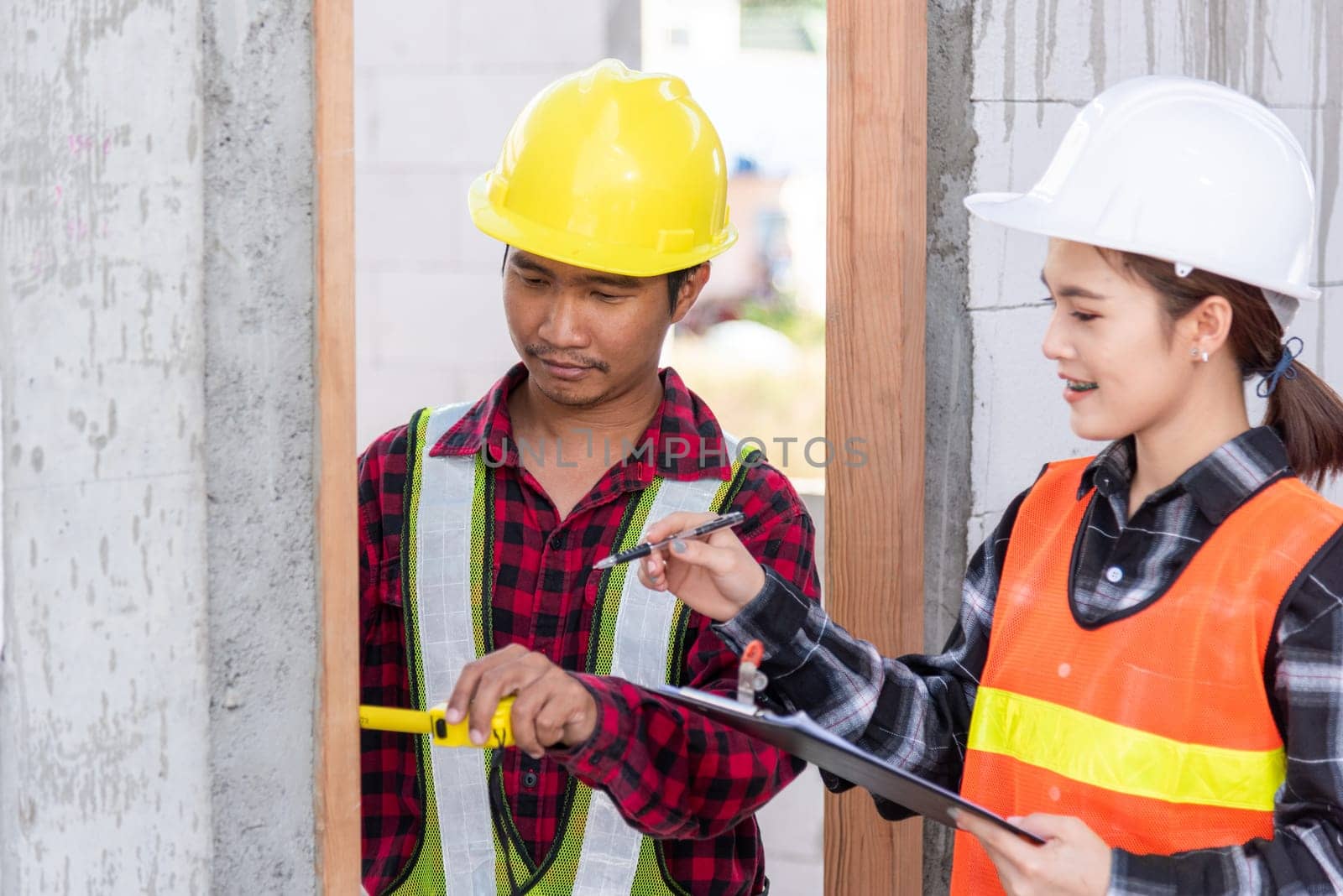 Male industrial builder workers installation process measuring wooden door with measure tape and service woman checking in building construction site. Worker work Building house concept