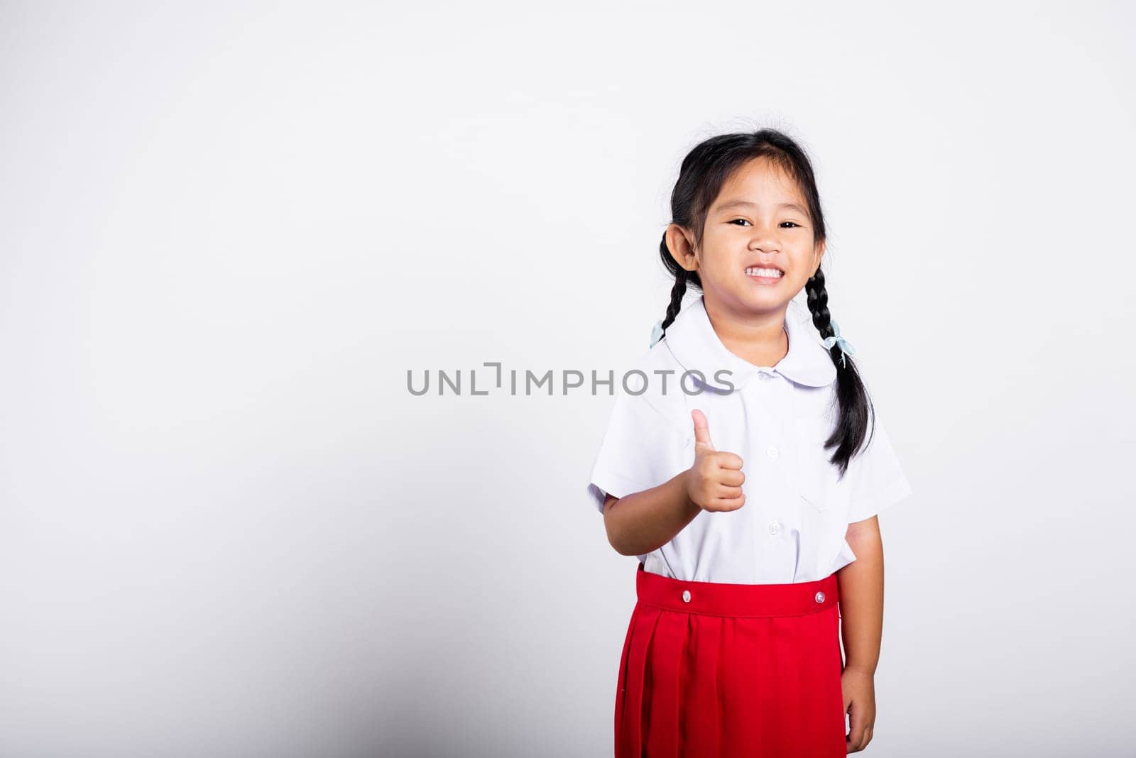 Asian adorable toddler smiling happy wear student thai uniform red skirt show thumb up finger in studio shot isolated on white background, Portrait little children girl preschool, Kid Back to school