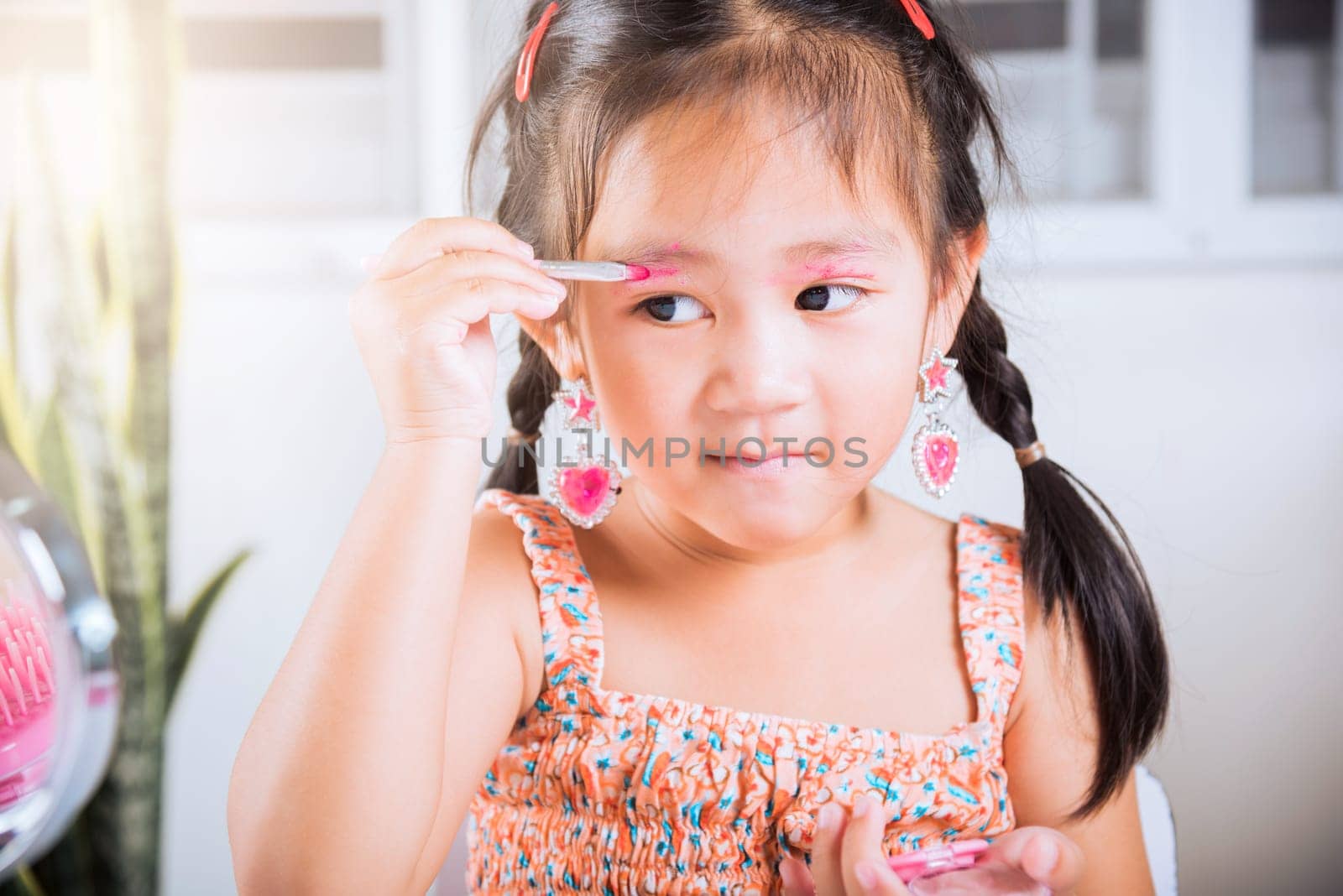 Happy kid is beautiful make up with cosmetics toy, Asian adorable funny little girl making makeup her face she applying carborundum eyeliner to eyelid, Learning activity to be woman at house