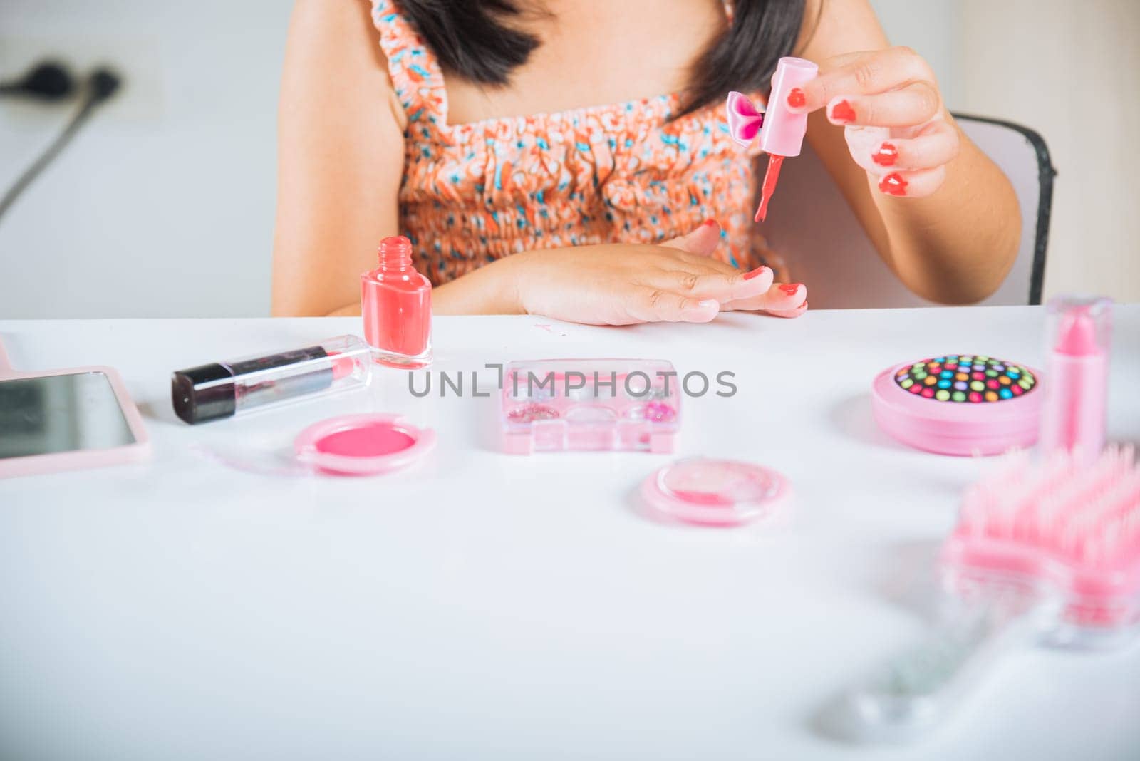 Asian adorable funny little girl making makeup dips brush into bottle to paints nails polish red nail varnish herself, Learning activity to be woman, happy kid is beautiful make up with cosmetics toy