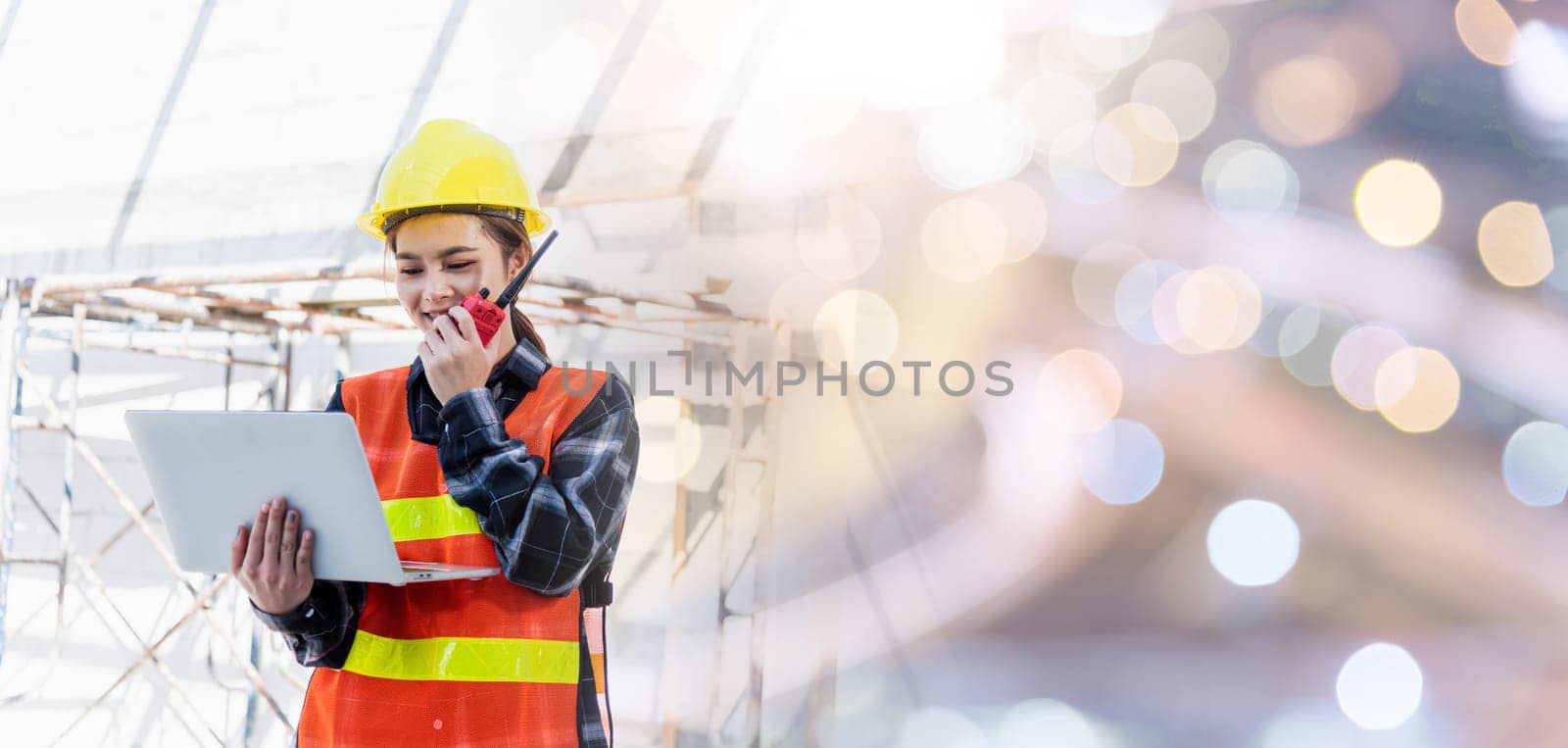 Asian engineer architect worker woman working at build construction site use laptop and talking with radio, engineering hold computer and radio discuss operate and control worker employee to building