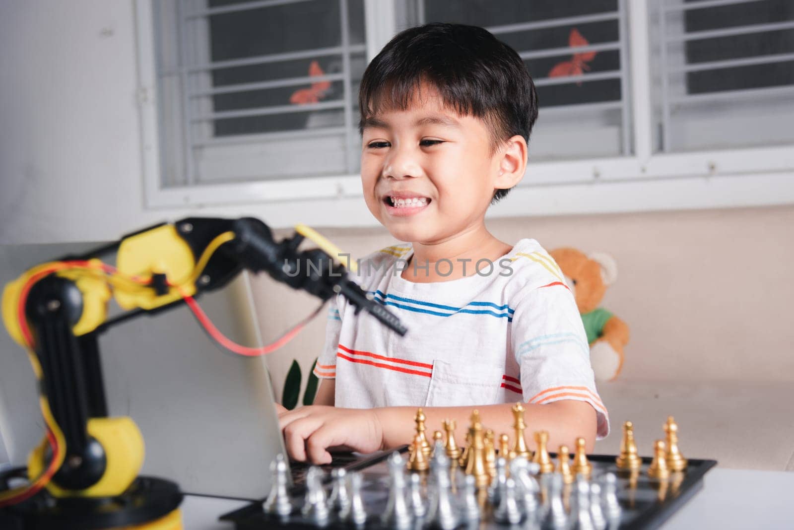 Asian little boy programming code to robot machine arm on laptop for play chess, STEM education E-learning, Funny children learning getting lesson control robot arm, Technology science education