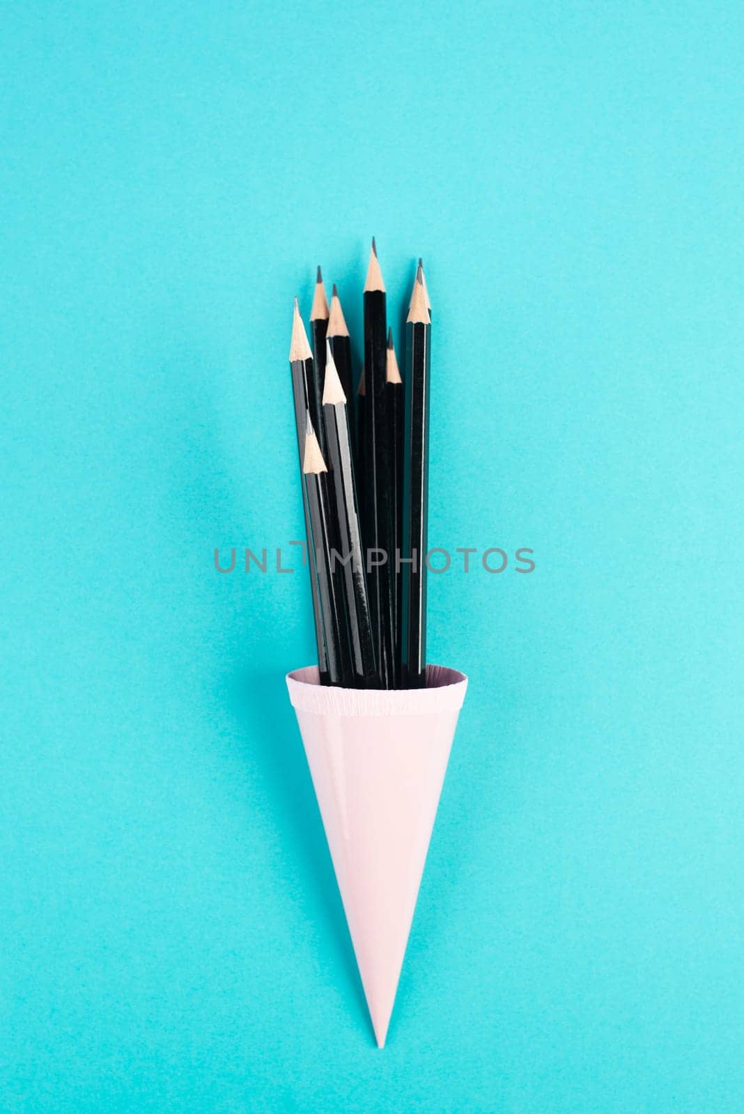 Black pencils in a cone on a blue background, minimalism, creative, surreal and education concept, copy space for text, pastel colored wall