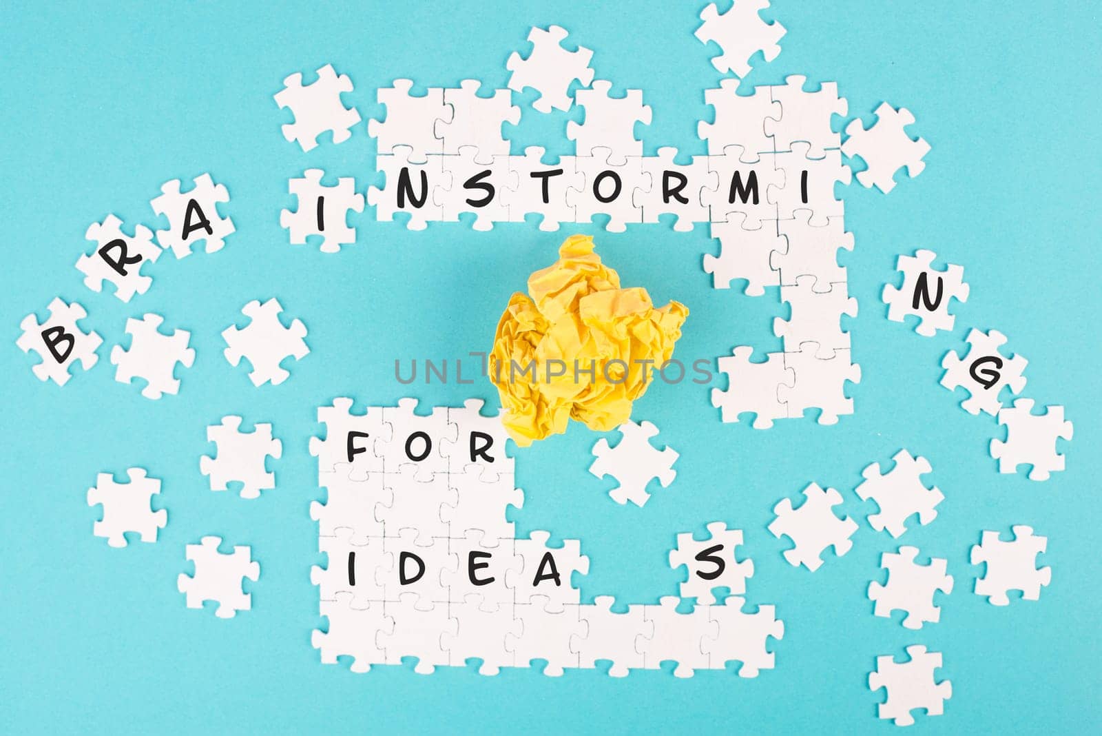 Puzzle on a blue background, yellow crumbled paper, words brainstorming for ideas are standing on the jigsaw pieces, business concept, working as a team together