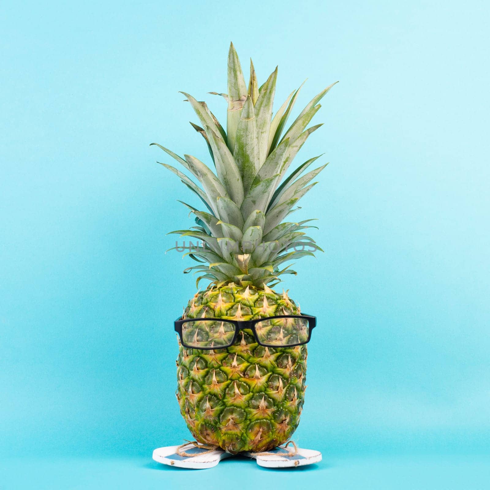 Pineapple with glasses and flip flops, vacation and travel concept, tropical summer holiday, funny fruit, blue background