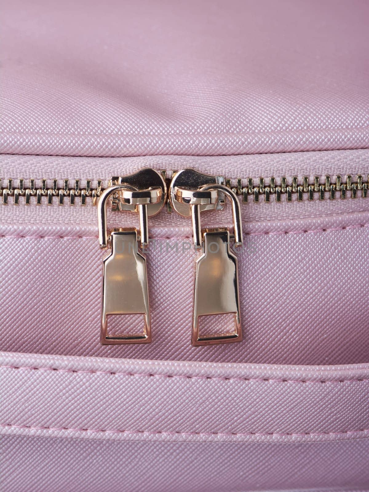 gold zippers with gold zippers are fastened on a pink leather object, close-up. High quality photo