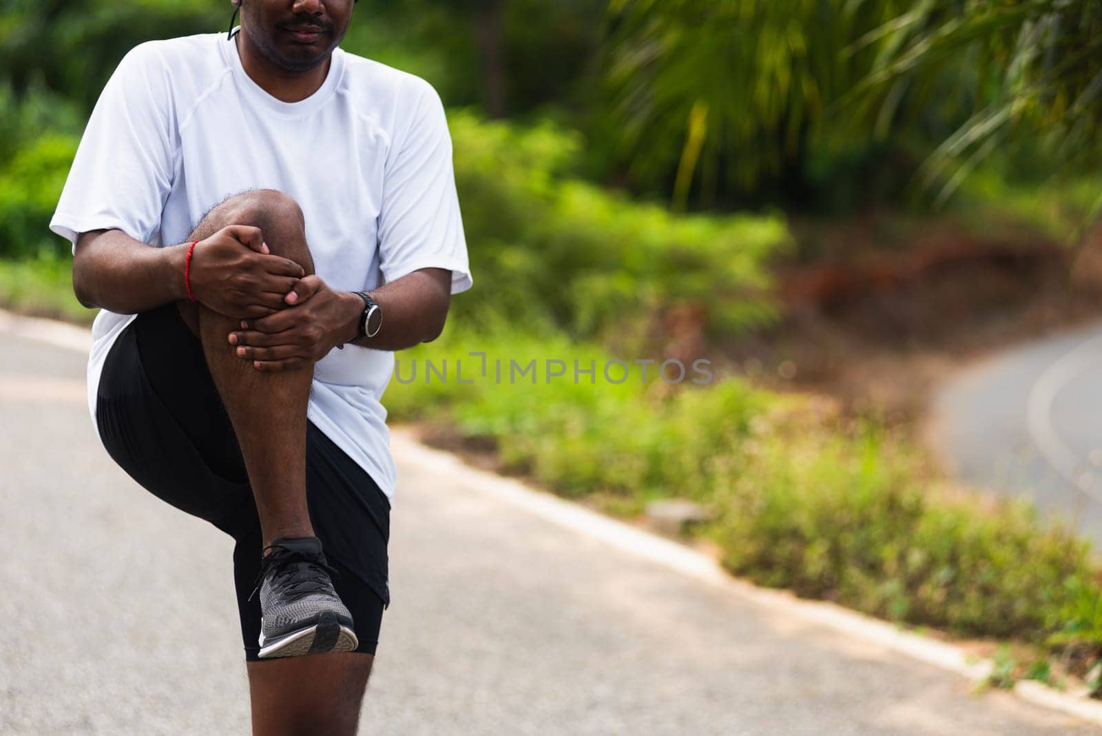 Asian young athlete sport runner black man standing wear feet shoe warm-up before run he stand to full lift single knee leg stretch to chest for running training at outdoor, healthy exercise workout