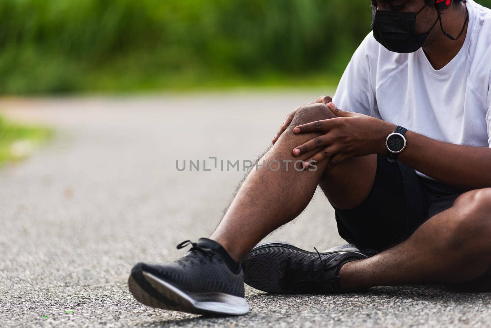 Close up Asian sport runner black man wear watch sitting he uses hands joint hold on his knee while running at the outdoor street health park, healthy exercise Injury from workout concept