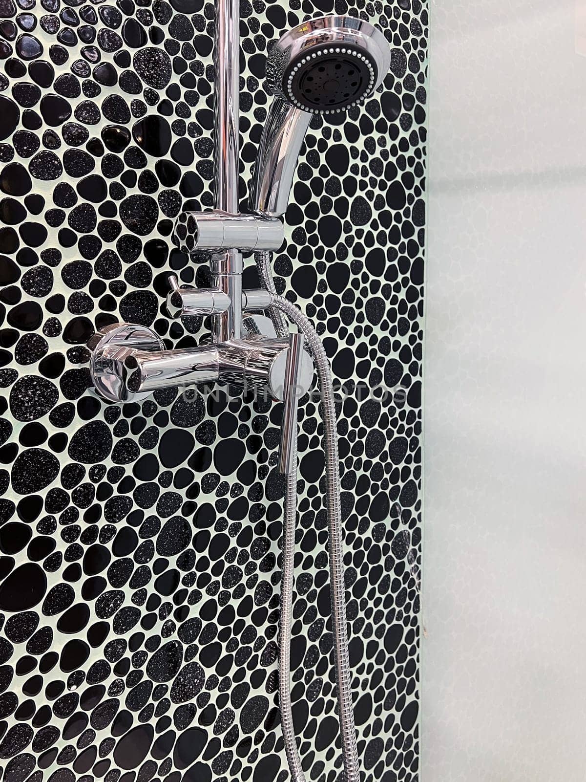 front view closeup of shower cabin with chrome head and faucet decorated with black pebbles