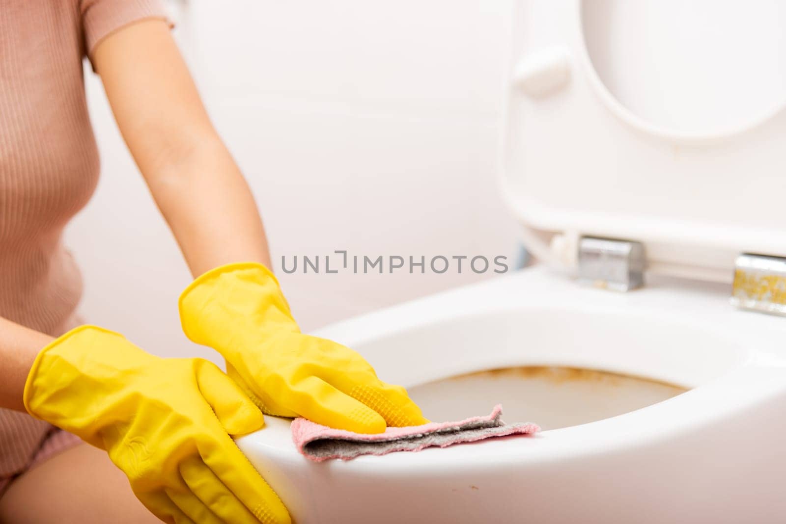 Hands of Asian woman cleaning toilet seat by pink cloth wipe restroom at house, female wearing yellow rubber gloves she sitting and cleanup or washing bathroom, Housekeeper healthcare concept