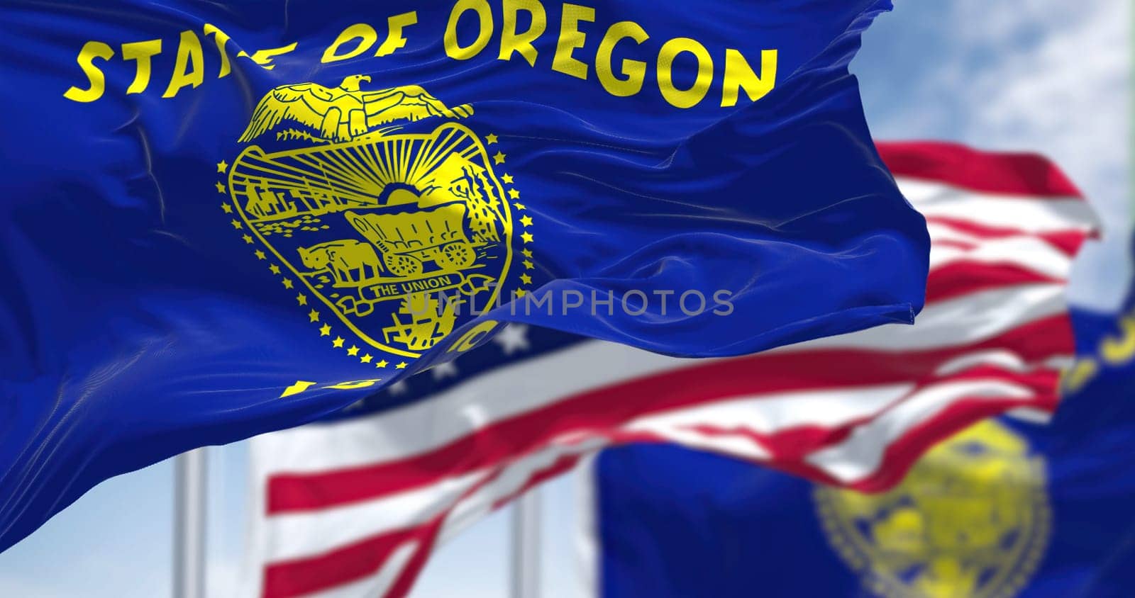The Oregon state flag waving along with the national flag of the United States of America. In the background there is a clear sky. Oregon is a U.S. state in the northwest