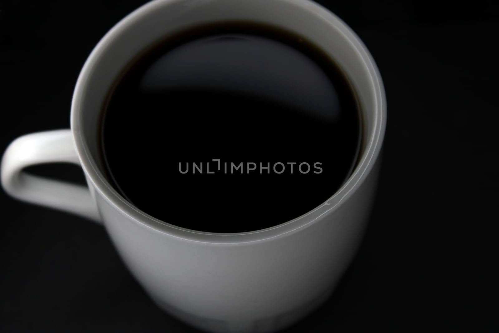 White mug with black coffee on a black background. View from above. Close-up..