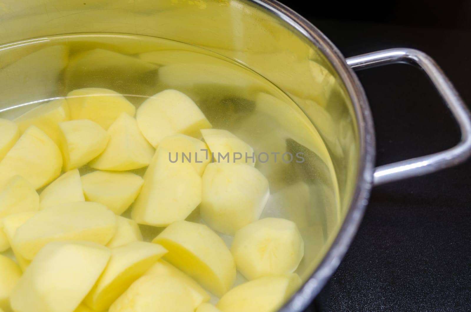 Pot filled with potatoes and water on a ceramic hob.