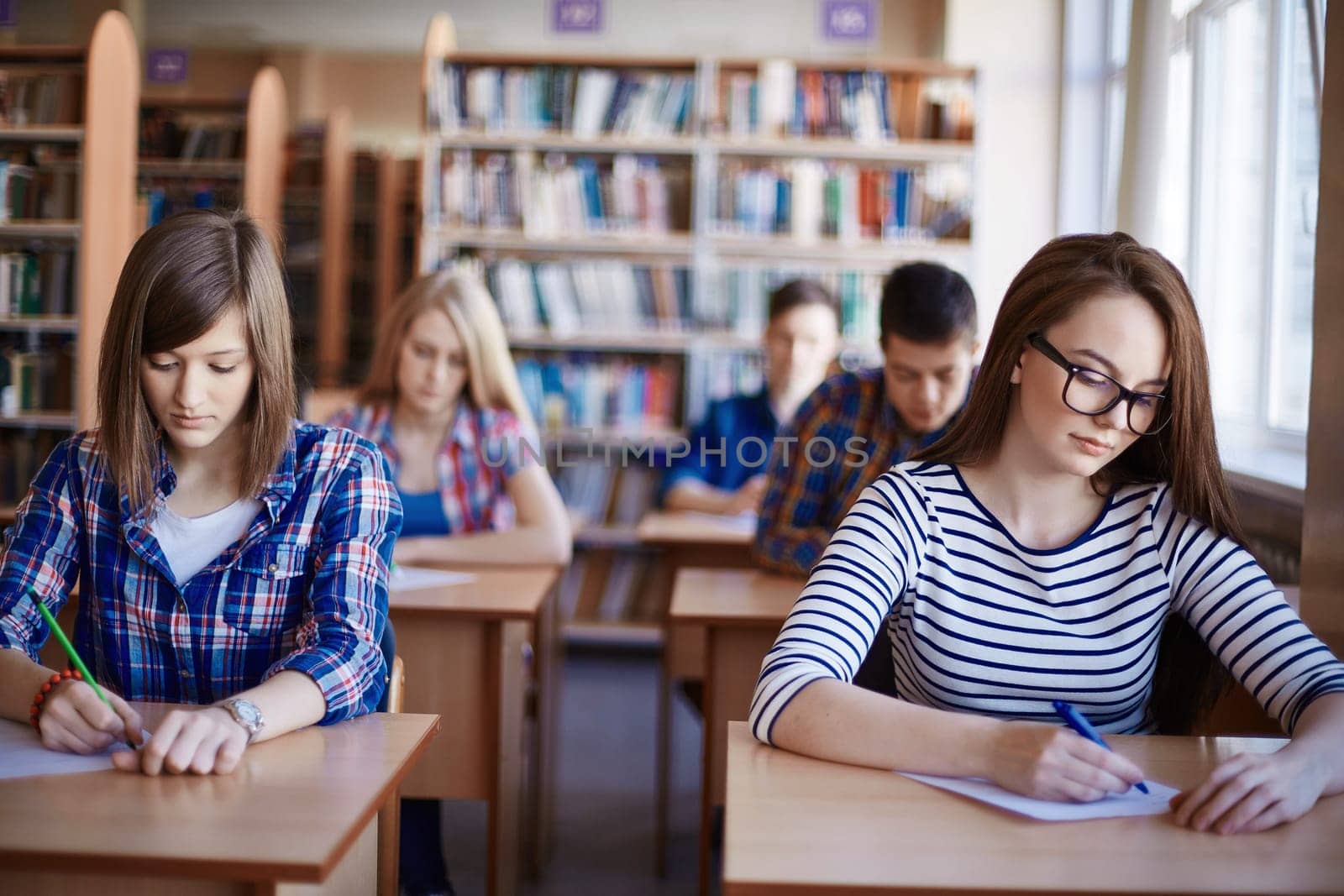 Clever girls sitting by desks and carrying out test at lesson