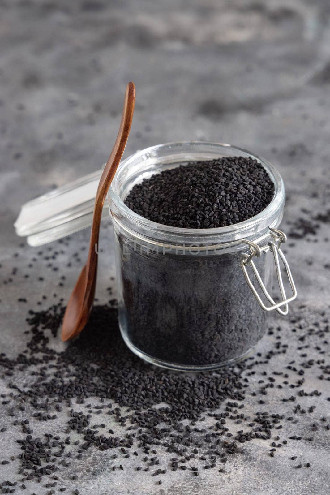 Indian spice Black cumin (nigella sativa or kalonji) seeds glass jar with a wooden spoon, close up. Traditional asian medicine, healthy and vegetarian food concept
