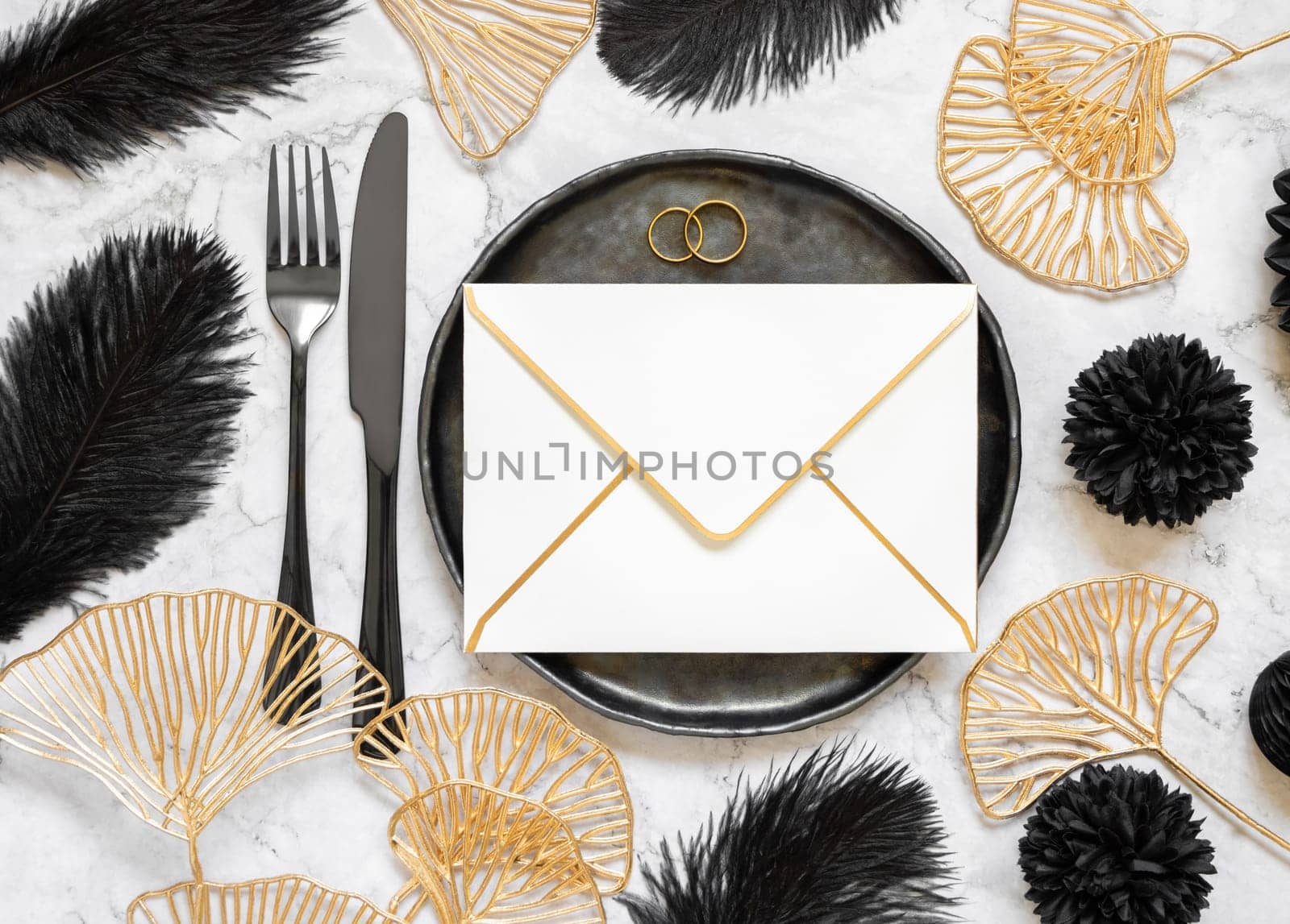 Black and golden wedding table setting with a blank envelope and rings top view, mockup. Elegant flat lay with horizontal greeting or Invitation paper envelope, wedding or holiday stationery template