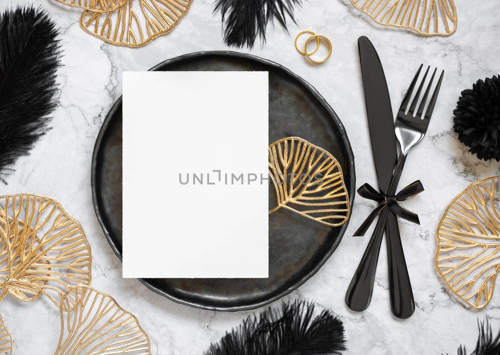 Black and golden wedding table setting with a blank card and rings top view, mockup. Elegant flat lay with vertical greeting or Invitation paper card, wedding or holiday stationery template
