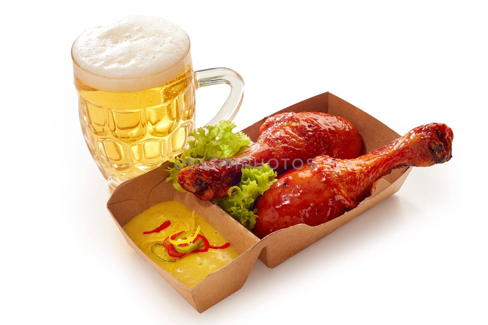 High angle of yummy BBQ chicken legs in sauce and mustard in paper container placed with glass of cold beer on white isolated background
