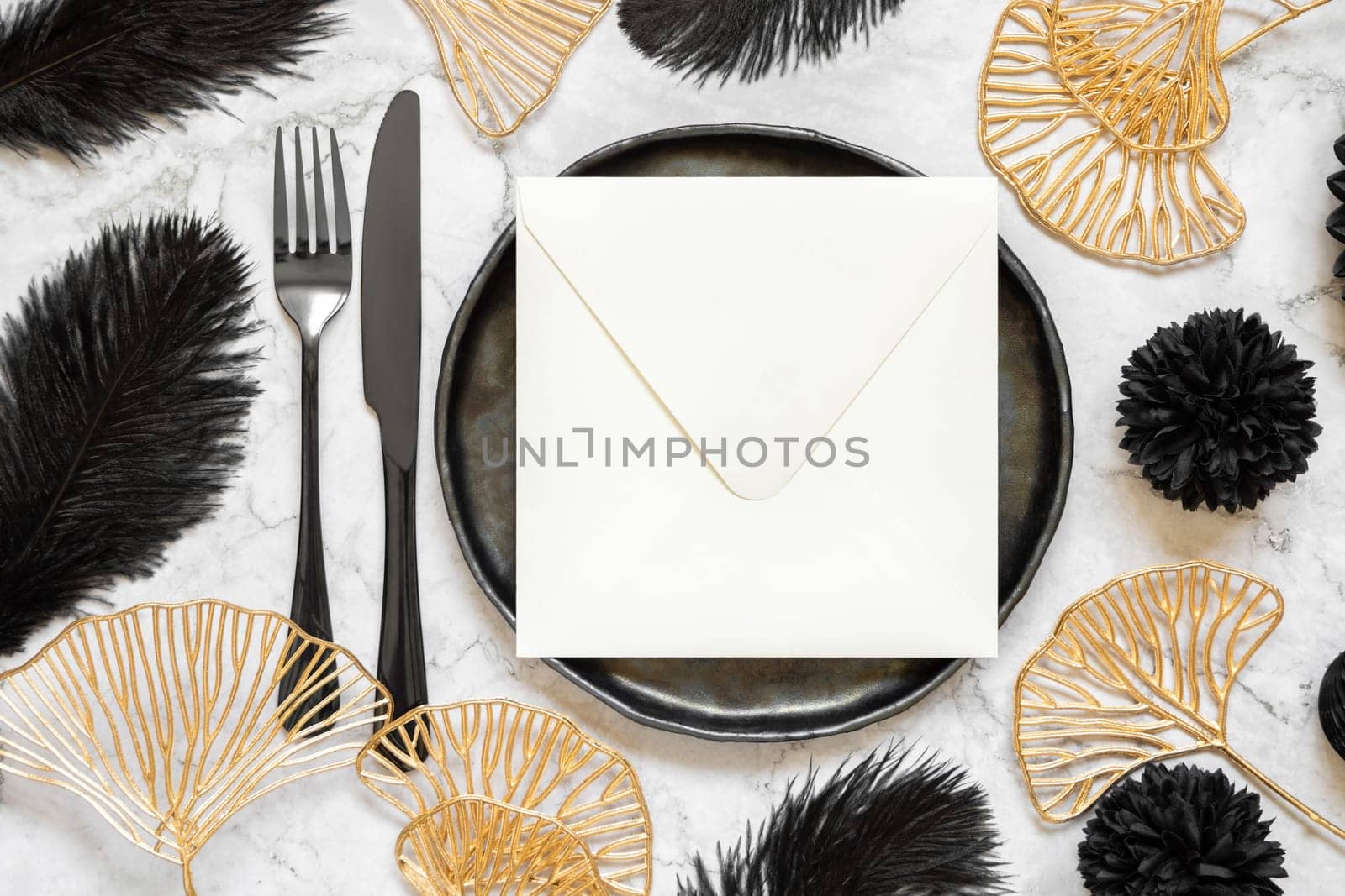 Black and golden wedding table setting with a blank square envelope top view, mockup. Elegant modern holiday flat lay, wedding or holiday stationery template