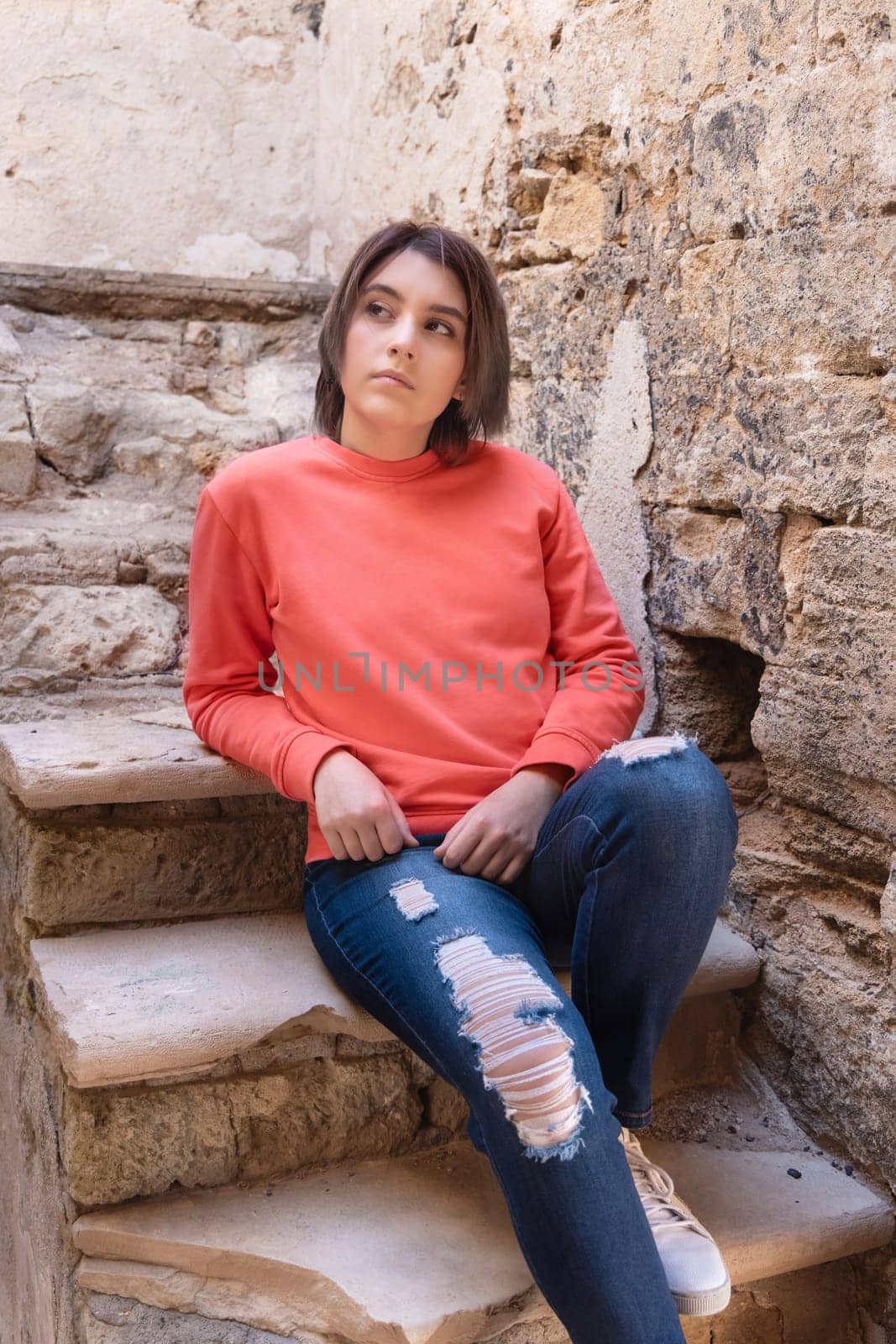 Teen girl wearing pink long sleeve shirt looking aside. Mockup. Serious Teenager girl sitting outdoor on a stairs spending her time alone. Adolescence concept