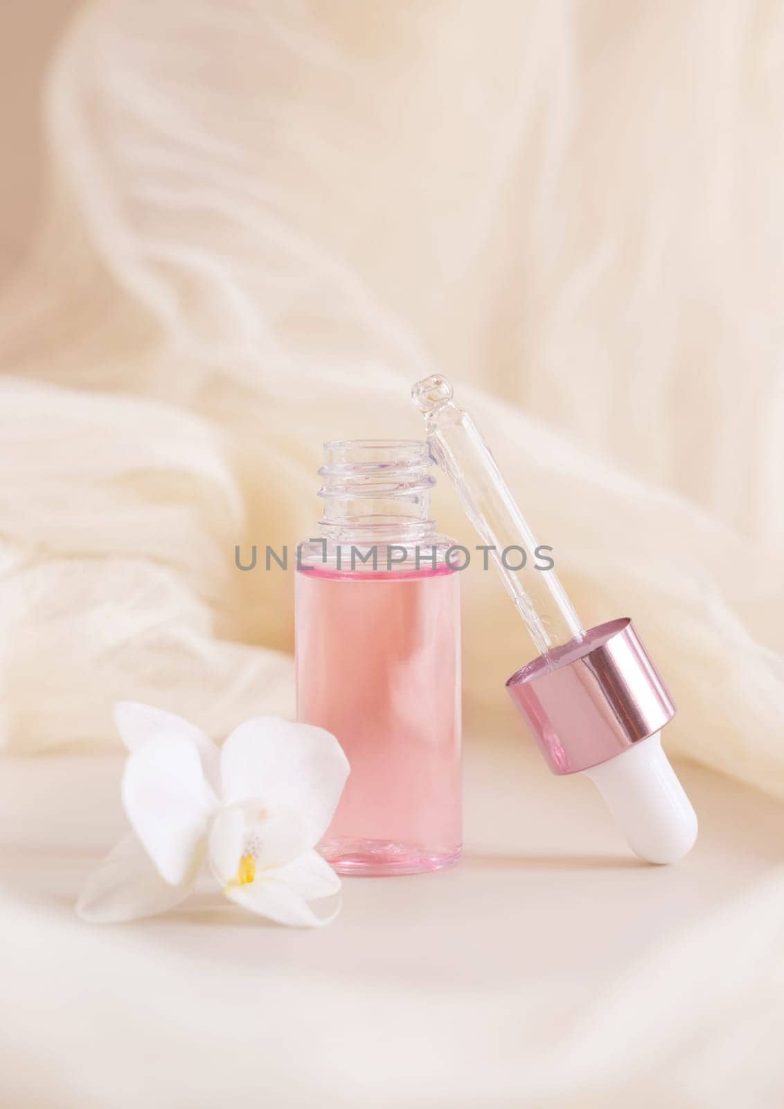 Light Pink opened Dropper Bottle near white orchid flower on light yellow, close up, mockup. Skincare beauty product, Aromatic oil or serum. Exotic cosmetics, pastel composition..
