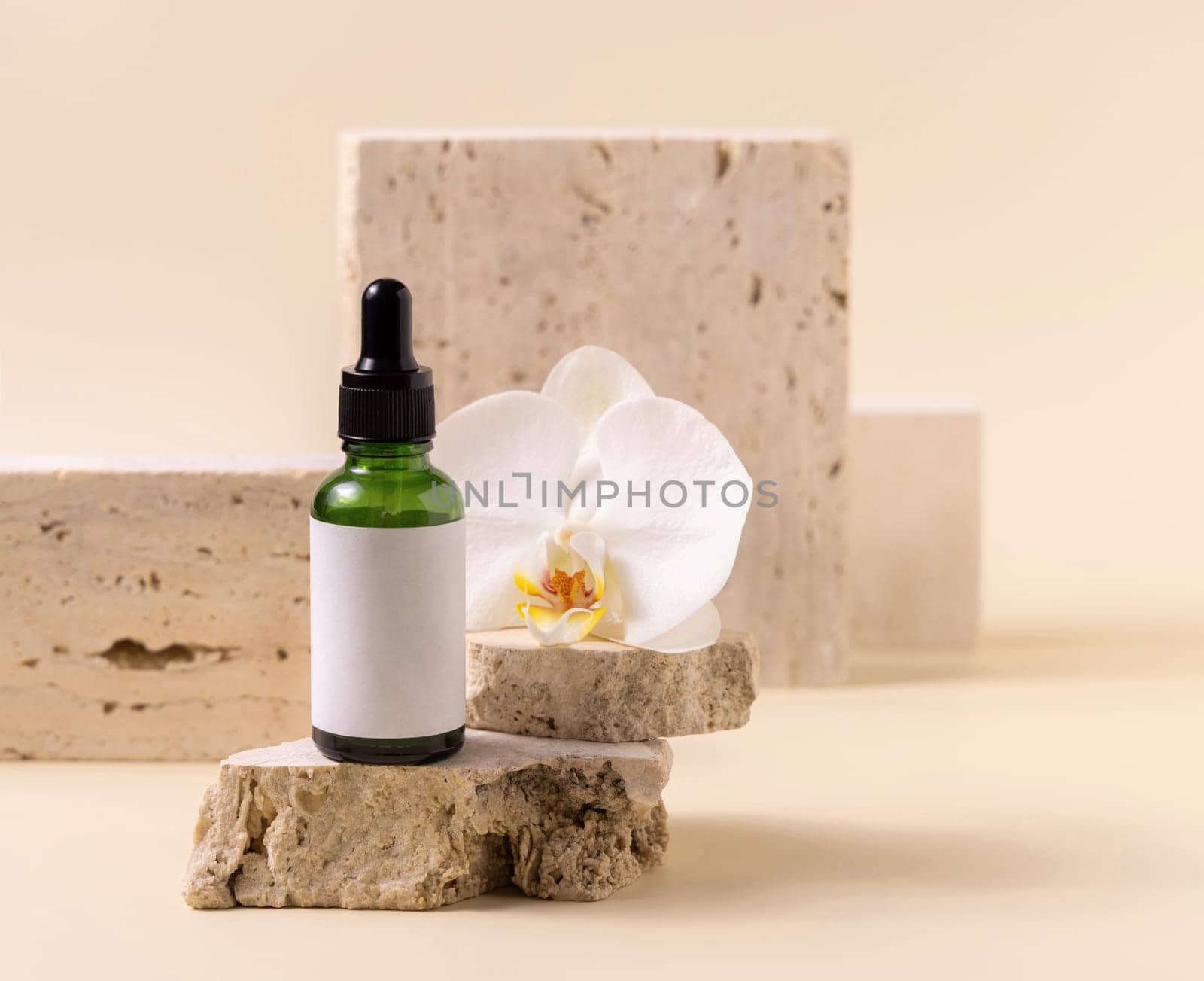 Green glass dropper bottle on stone near white orchid flower on light yellow, close up, mockup. Skincare handmade beauty product, serum or lotion. Exotic natural cosmetics..