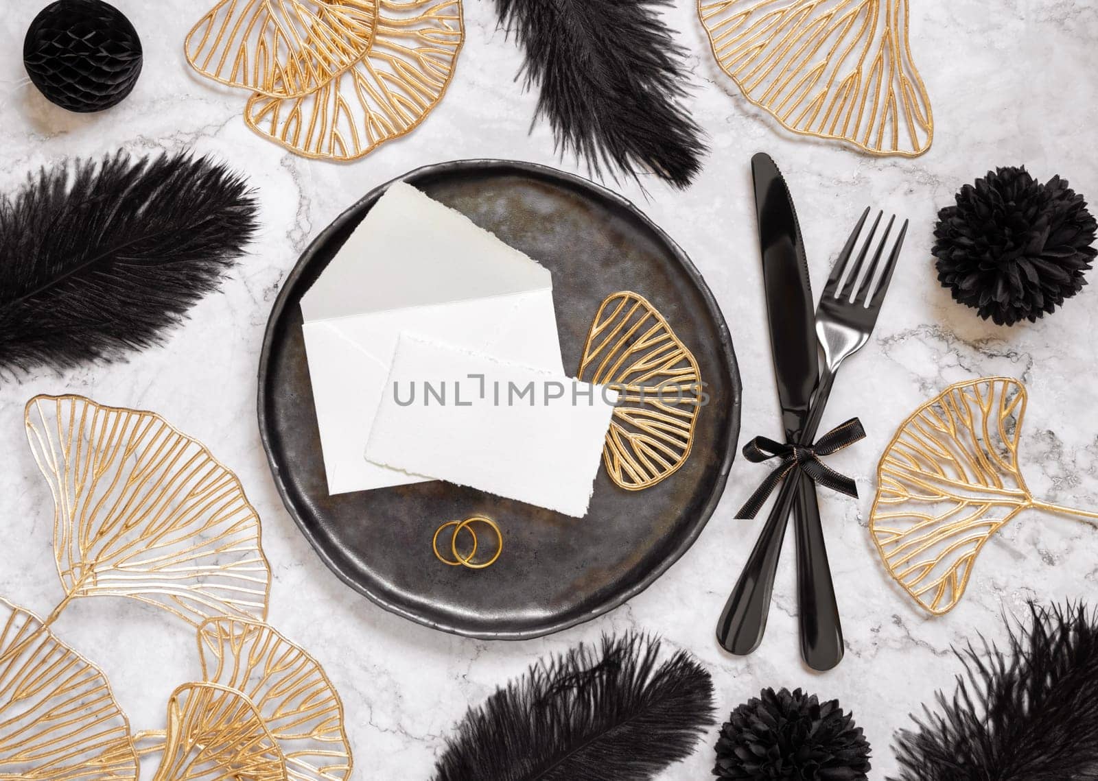 Black and golden wedding table setting with a place card and rings top view, mockup. Elegant flat lay with paper card and envelope, wedding or holiday stationery template