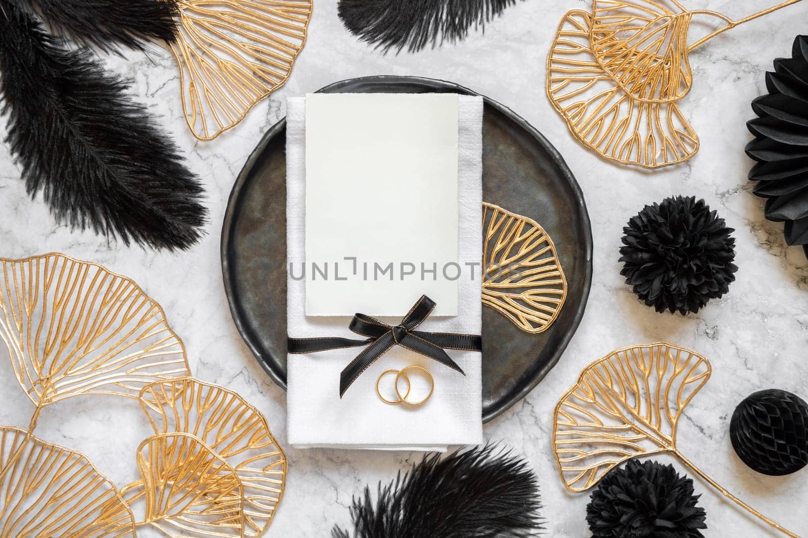 Black and golden wedding table setting with a blank card and rings top view, mockup. Elegant flat lay with vertical Invitation paper card, wedding or holiday stationery template