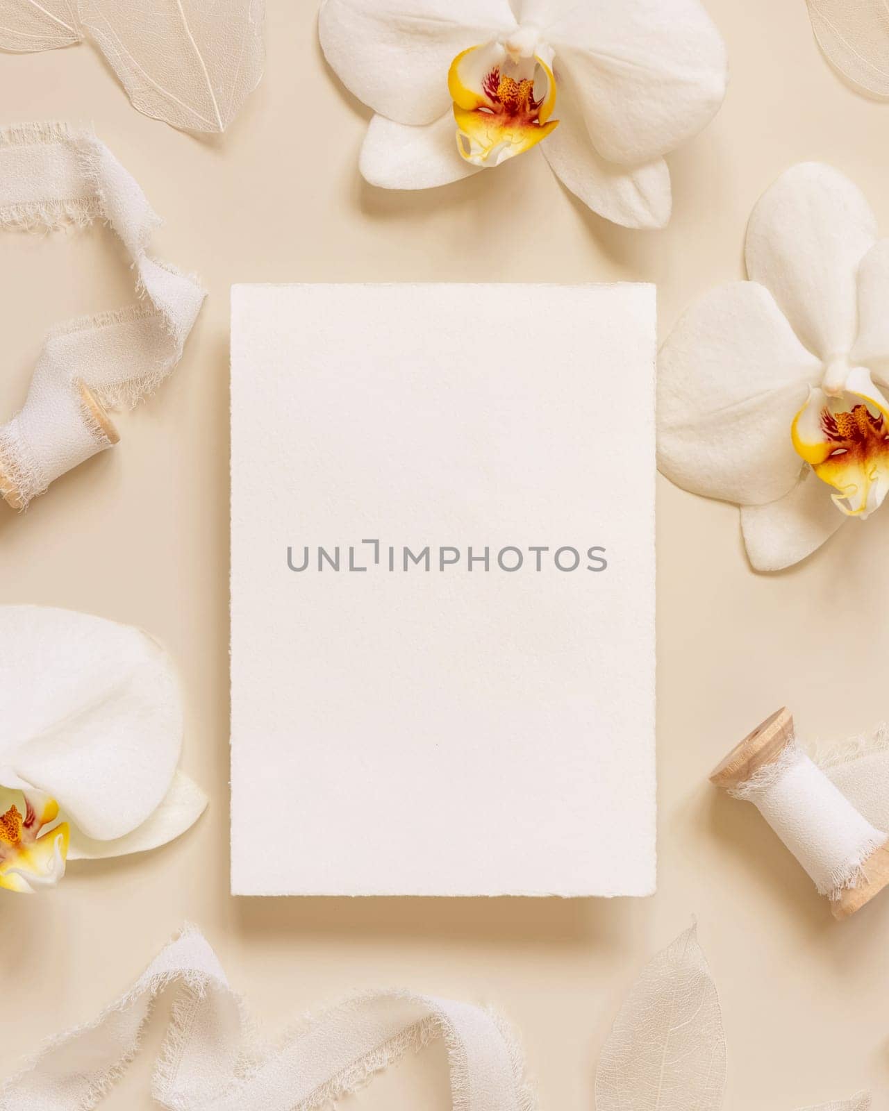 Wedding Card near white orchid flowers and silk ribbons on light yellow top view, mockup. Romantic scene with vertical blank card flat lay. Valentines or Spring romantic concept