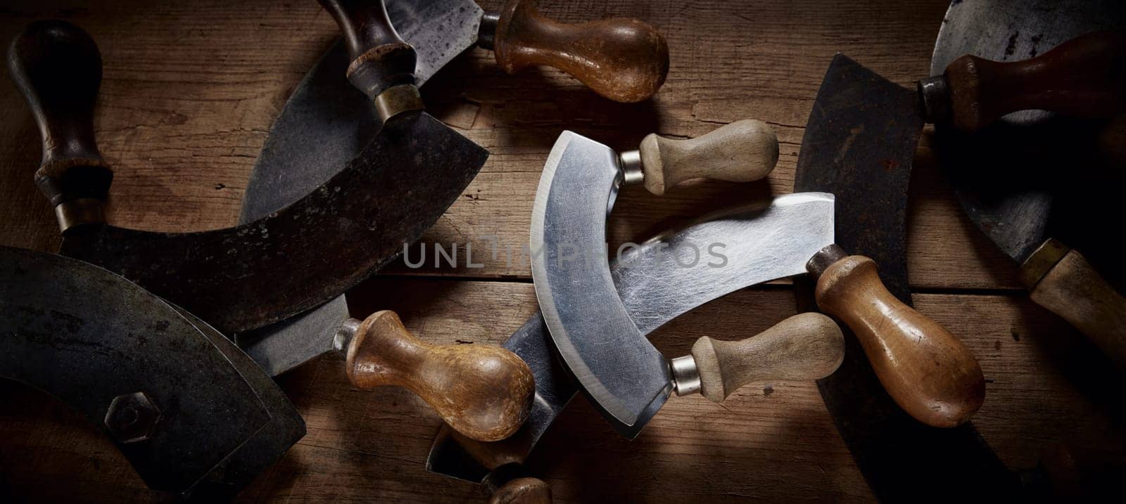 Top view of collection of old fashioned mezzaluna knives with curved blades and wooden handles placed on table in kitchen