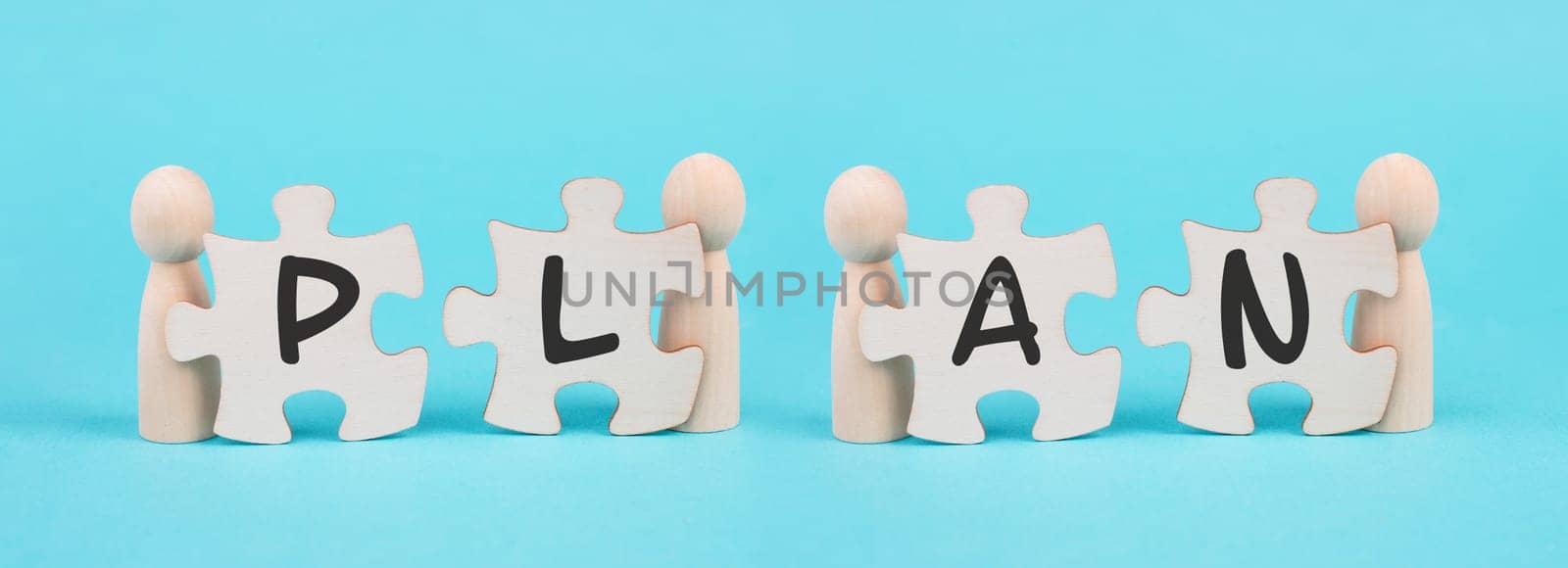 The word plan is standing on puzzle pieces, connect the parts together, corporate in teamwork, cooperating to reach a goal