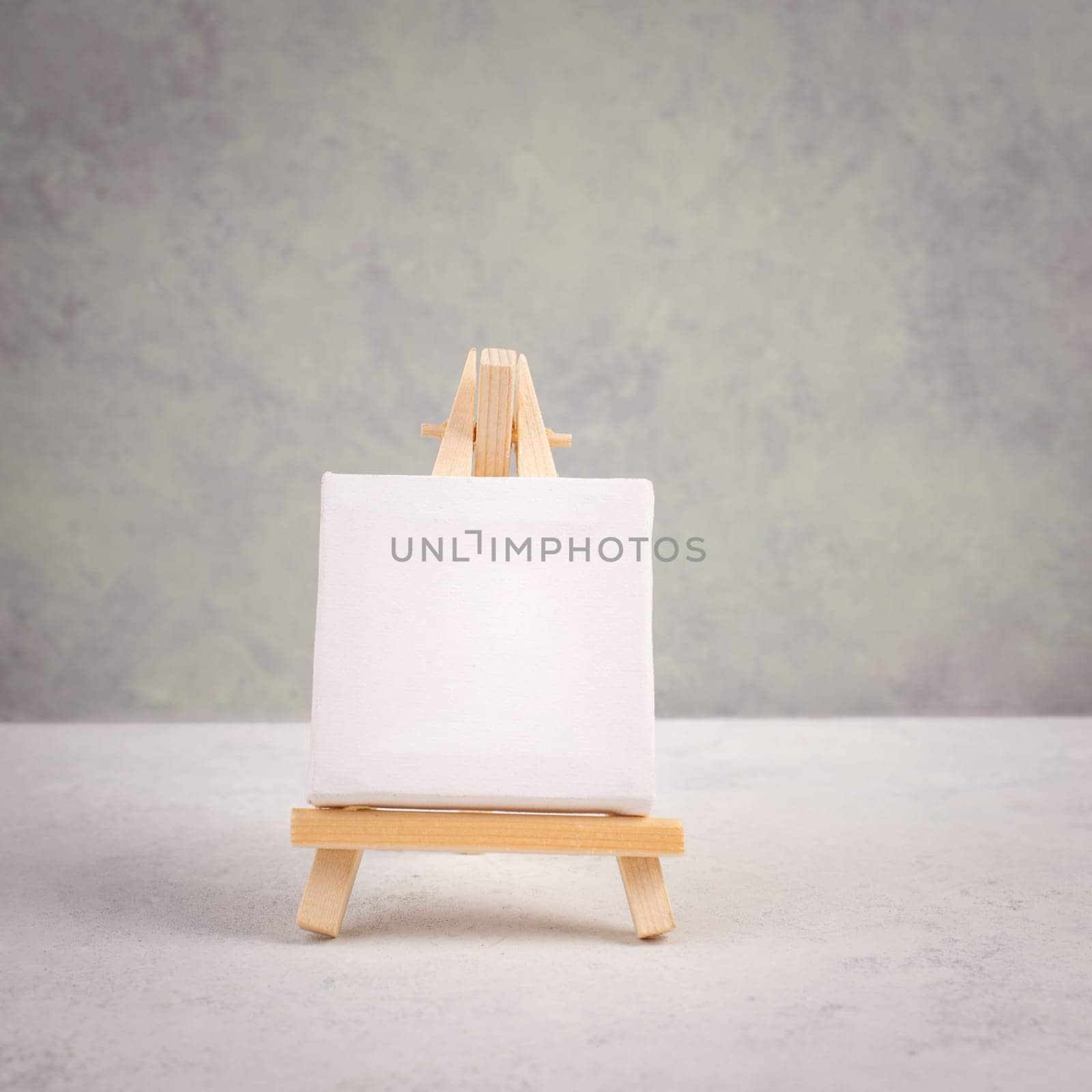 Easel with blank white canvas in front of a gray textured background, frame to add paintings and pictures