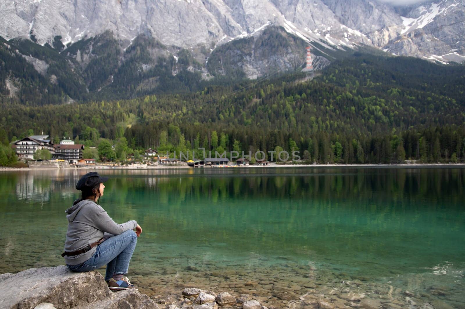 Tourist sitting on a rock and watching a beautiful view over lake Eibsee in the Bavarian Alps. Famous touristic destination in Europe