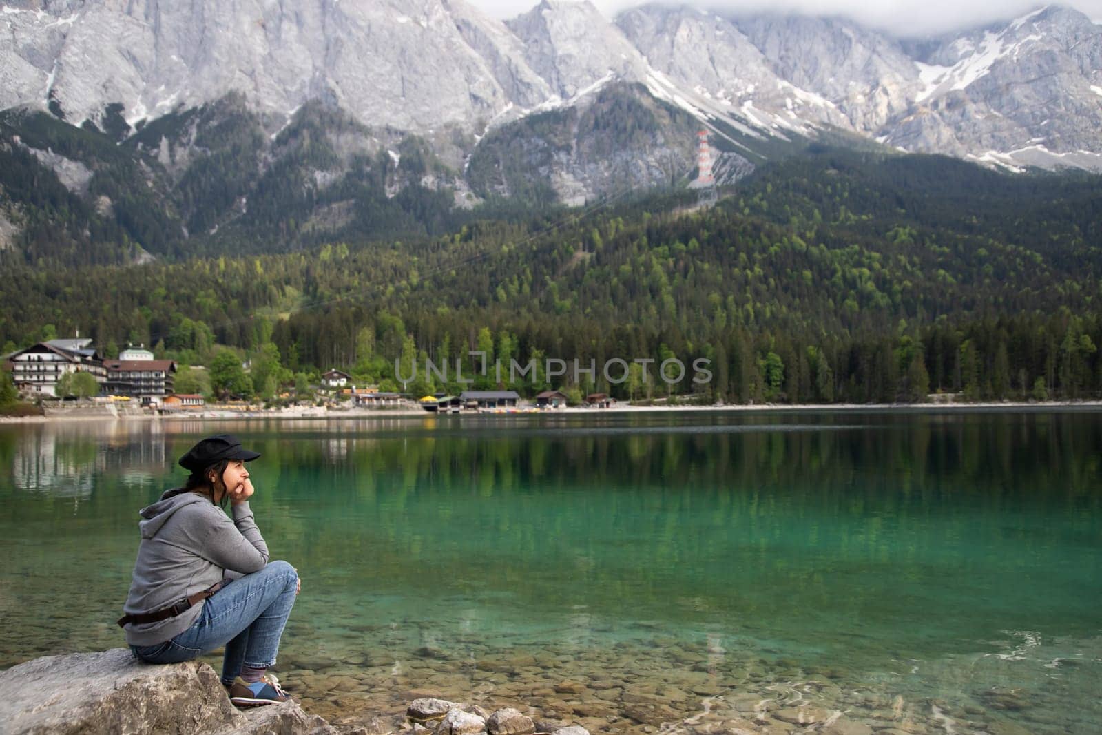 Tourist sitting on a rock and watching a beautiful view over lake Eibsee in the Bavarian Alps. Famous touristic destination in Europe