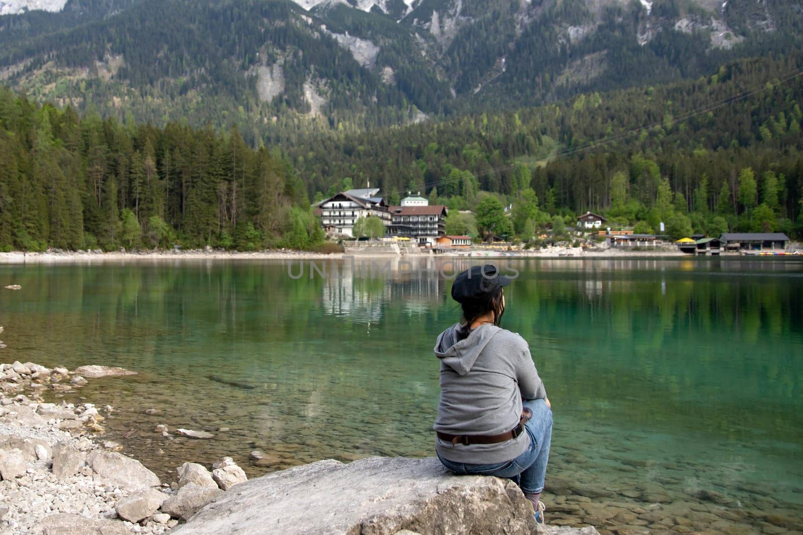 Tourist sitting on a rock and watching a beautiful view over lake Eibsee in the Bavarian Alps. Famous touristic destination in Europe